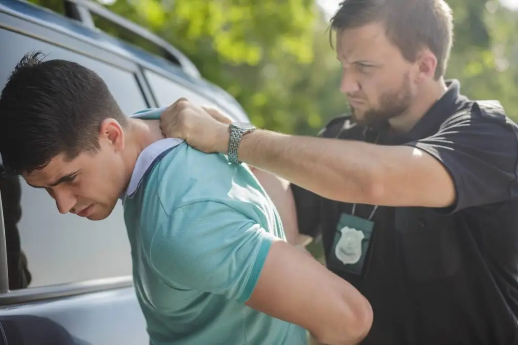 police officer arresting a man with his head against a vehicle
